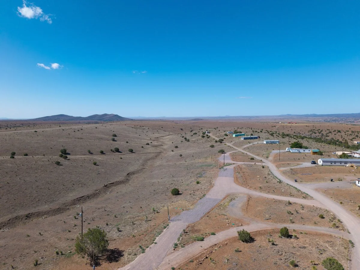 Aerial view of a Whiskey Creek Mobile Estates with a small residential area and unpaved roads under a blue sky with a few clouds.