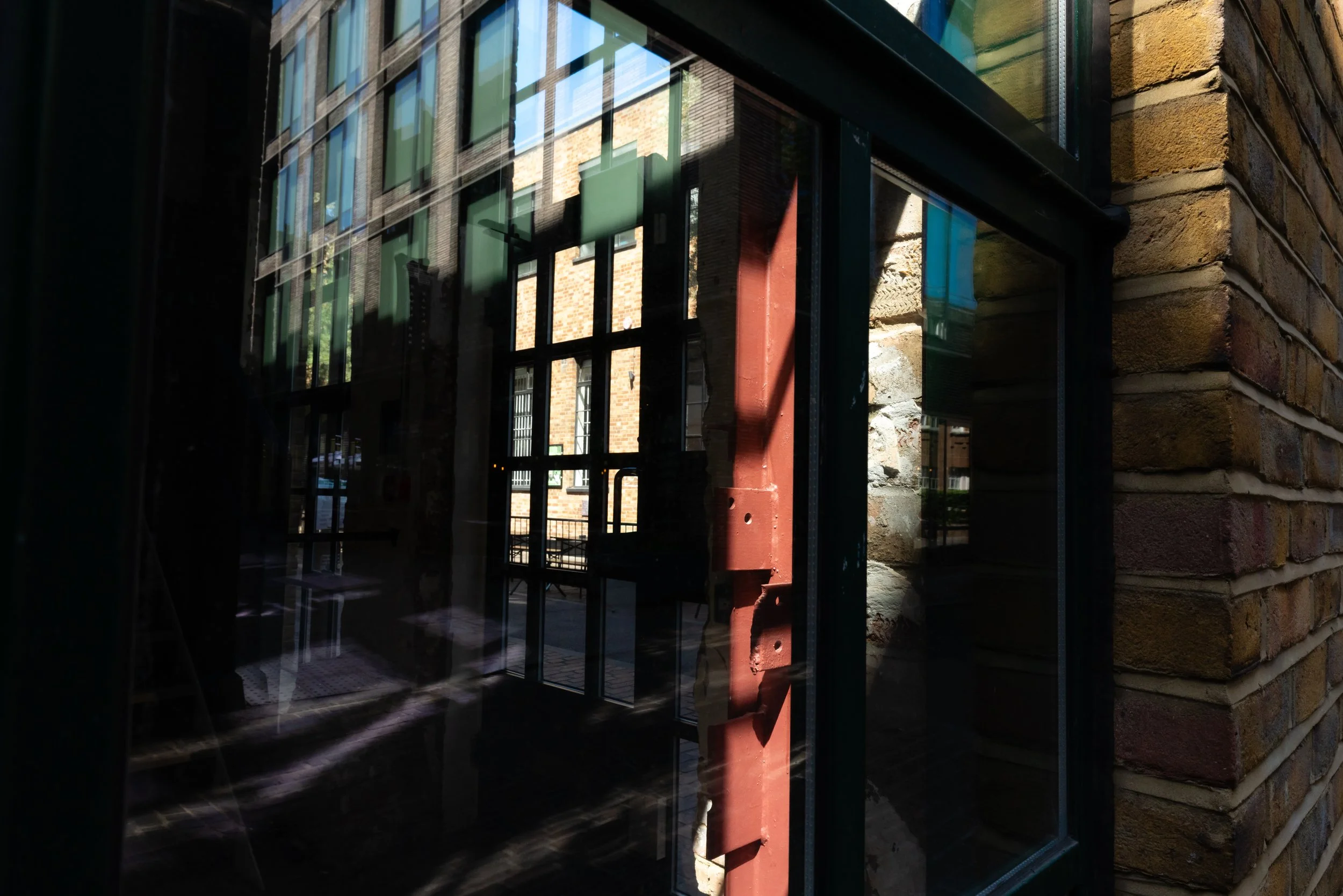 Reflective glass window on a brick building, with a garden scene reflected in the glass and a red pipe near the window.
