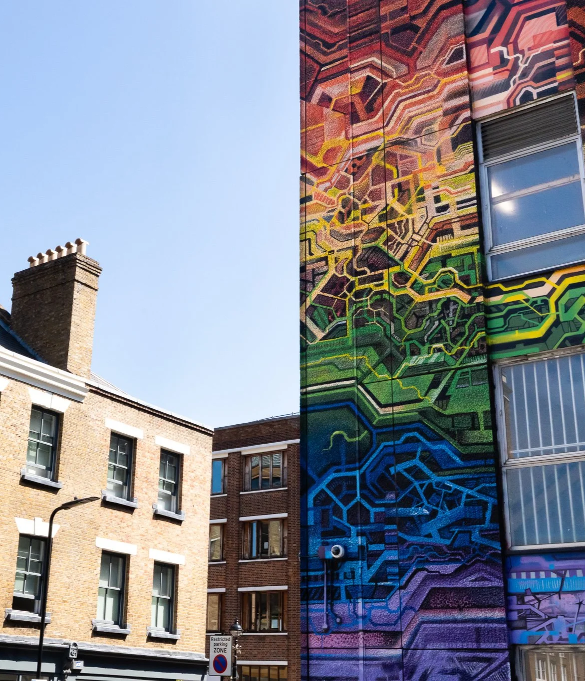 Colorful abstract mural painted on the side of a tall building in an urban area.