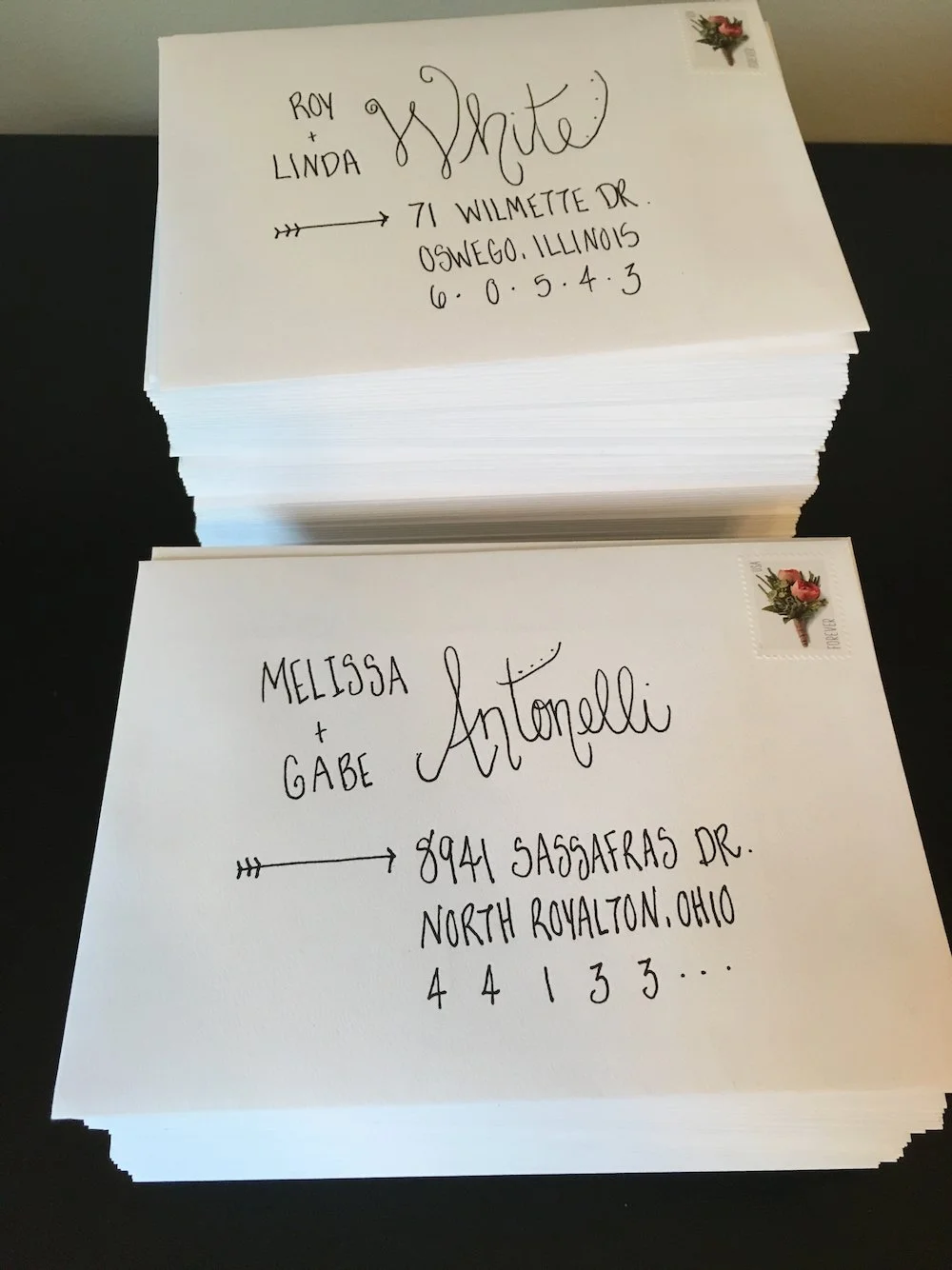 Stack of white envelopes with handwritten addresses, stamps in the upper right corner, and decorative handwriting style.