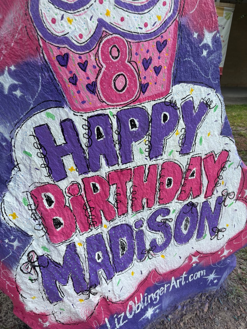 Colorful birthday sign with a cupcake illustration, the number 8, and the message 'Happy Birthday Madison'. Mixed pink, purple, and white colors with glitter and star decorations.