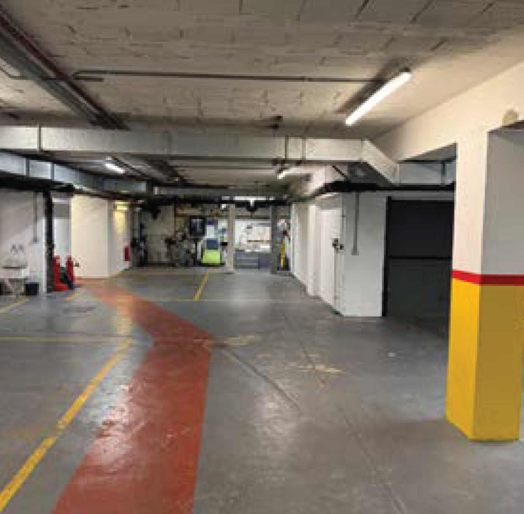 Underground parking garage with a yellow striped barrier, concrete walls, and ceiling pipes and lights.
