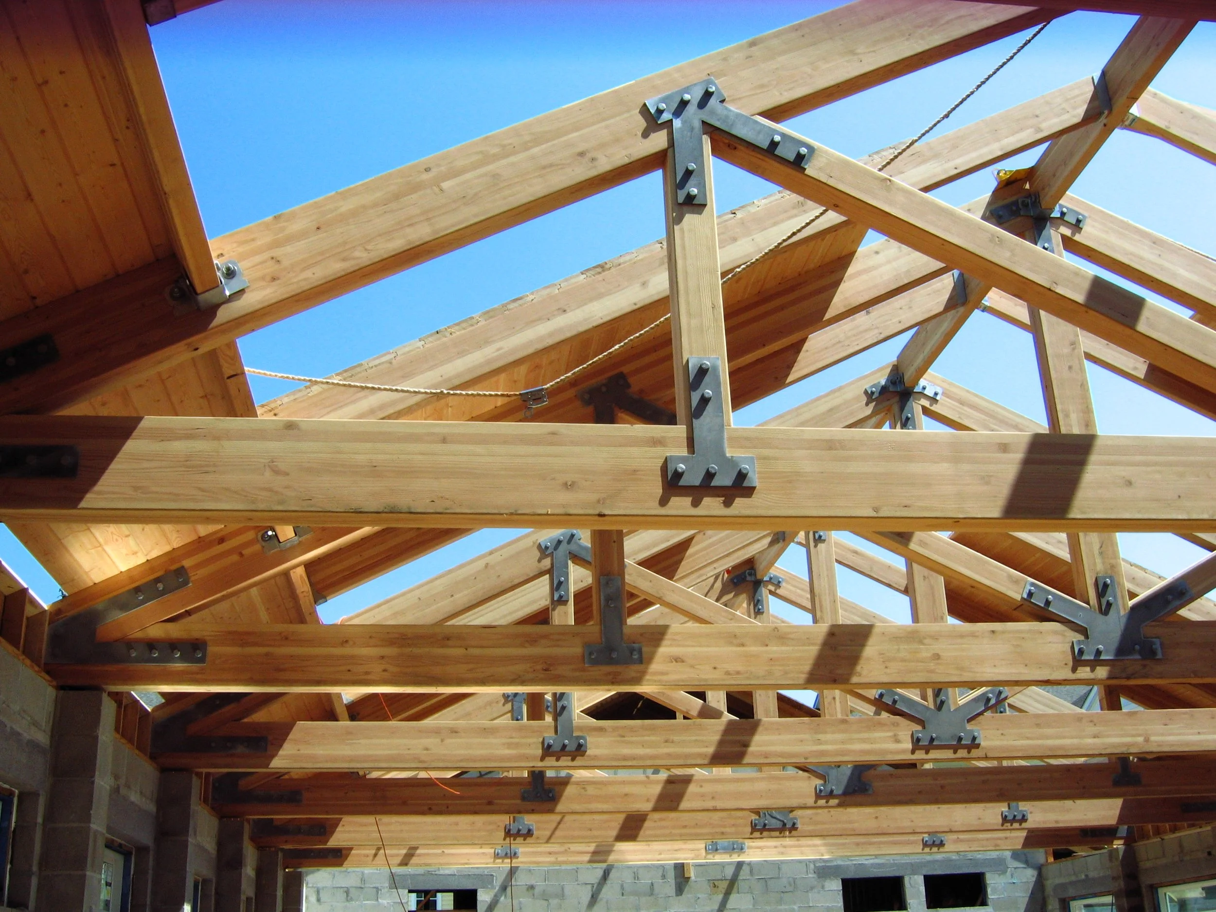A wooden construction framework with beams and metal brackets, set against a clear blue sky.