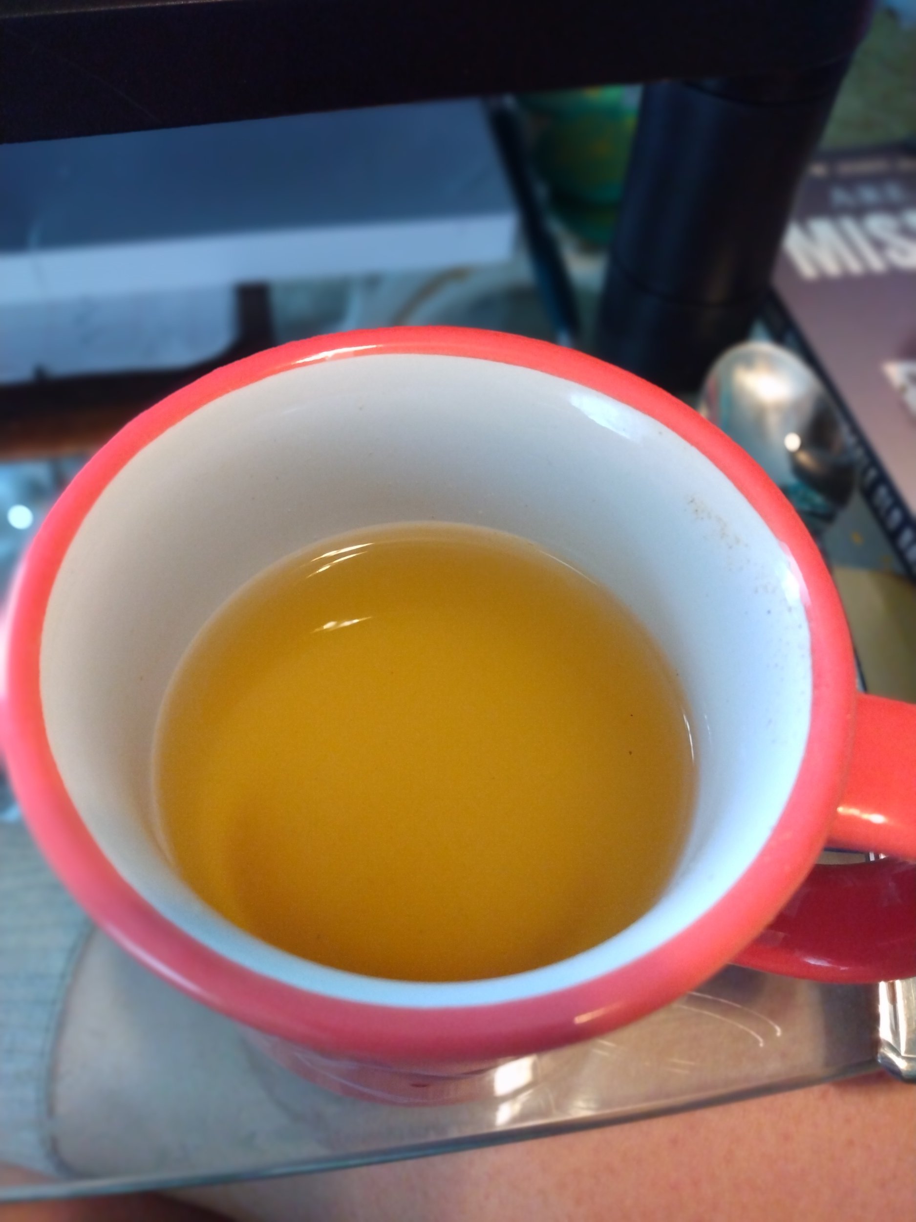 Close-up photo of a red mug filled with a yellowish beverage, placed on a reflective surface.