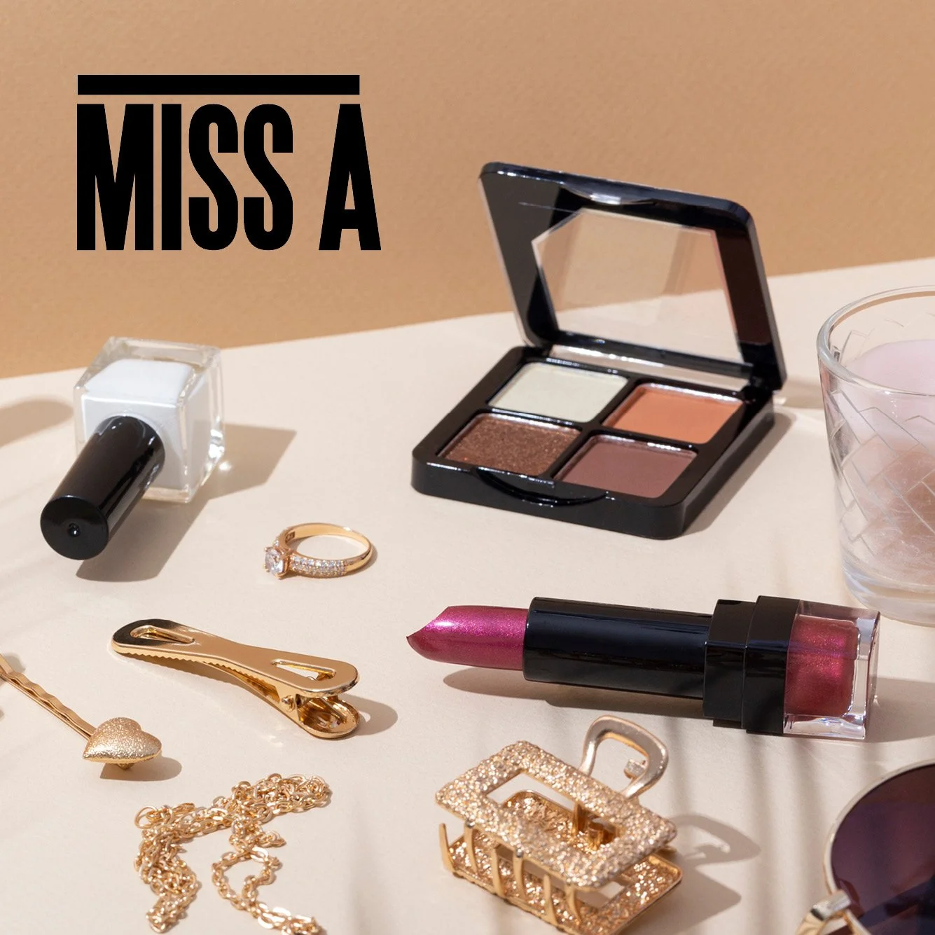 Styled image of cosmetics and jewelry, alongside, the Miss A logo