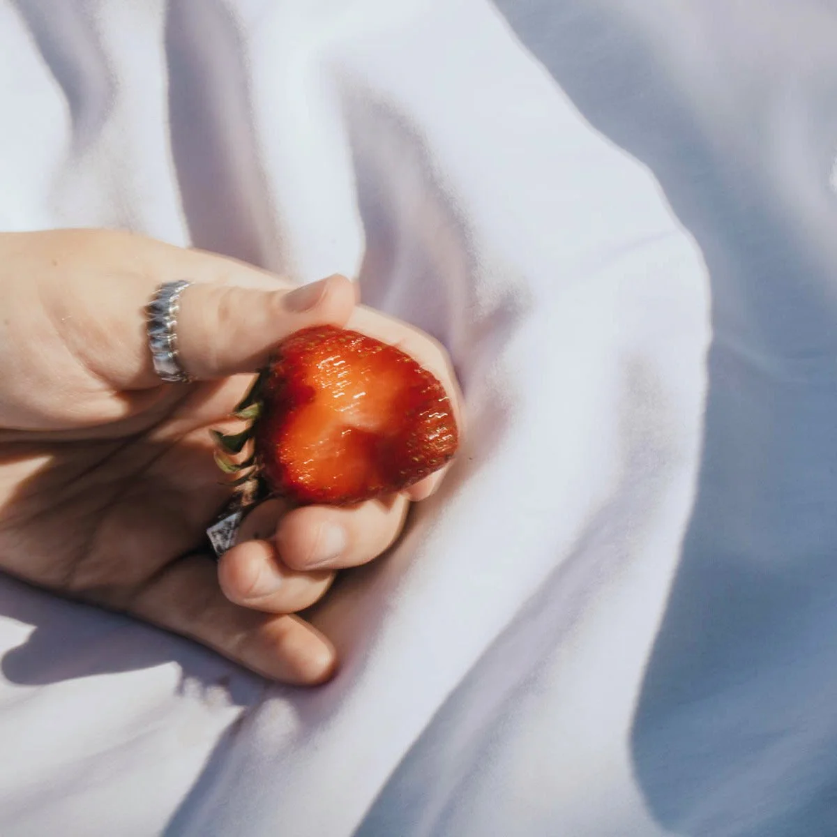 A hand holding a halved strawberry on a white fabric background.