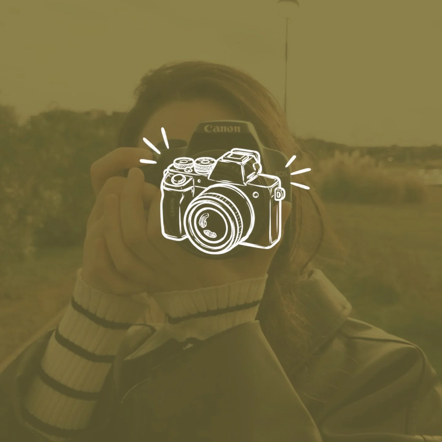 A person taking a photo outdoors during sunset or sunrise, with a landscape of trees and a road in the background. The person is wearing a hat, gloves, and a jacket, and is holding a camera.