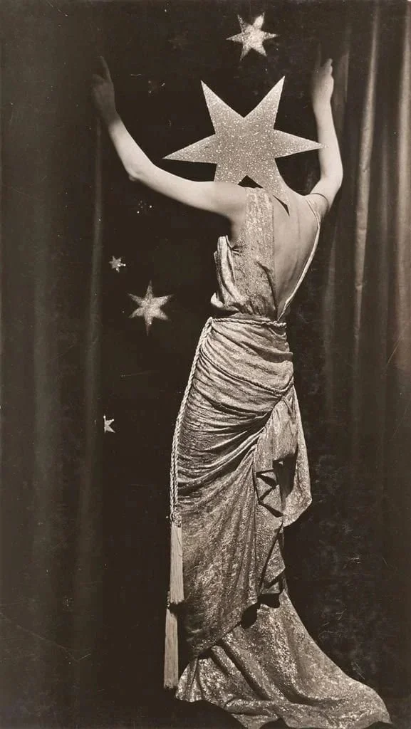 A person dressed as a starry cosmic figure, wearing a draped gown, in front of a backdrop decorated with star shapes.