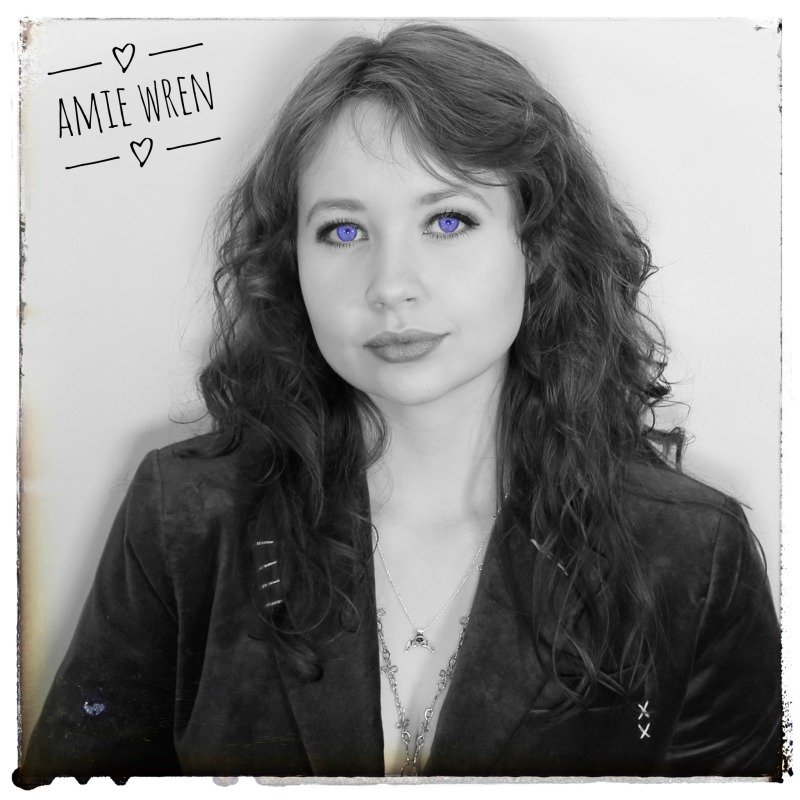 A black and white portrait of a young woman (Amie) with curly hair and blue eyes, wearing a dark blazer and layered necklaces, looking directly at the camera. A handwritten note in the upper left corner says 'Amie Wren' with hearts above and below.