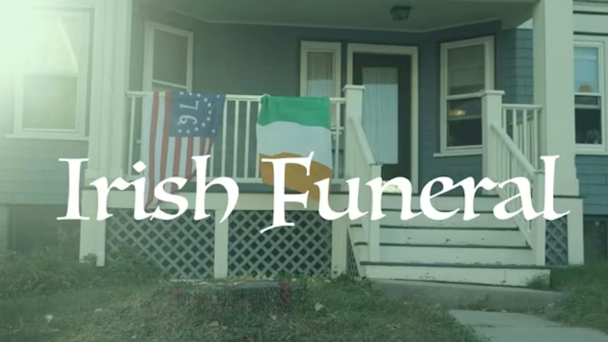 Front porch of a house with Irish and American flags hanging on the railing, and text overlay reading 'Irish Funeral'.