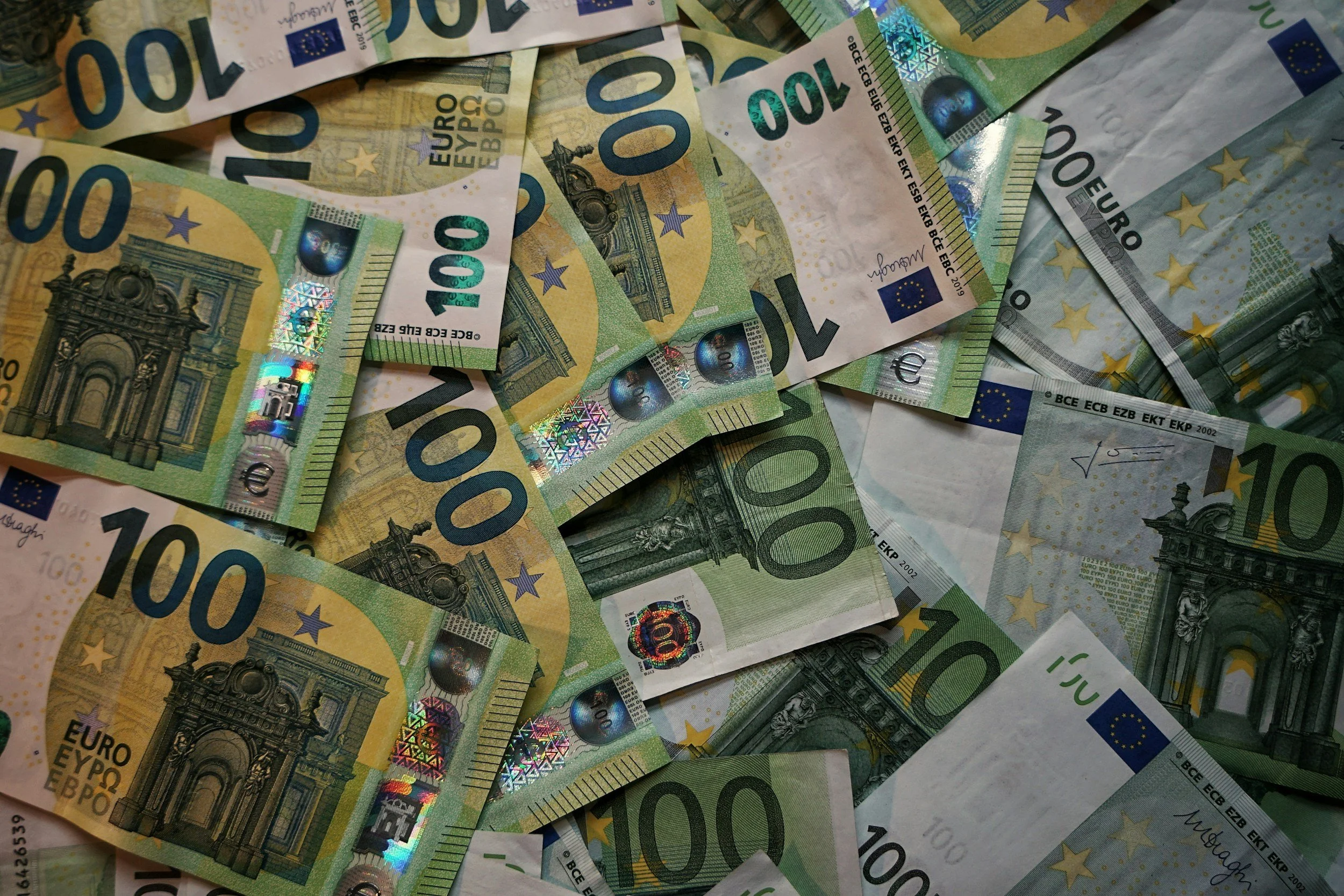Several 100 Euro banknotes fanned out and overlapping on a surface.
