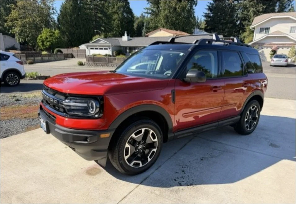 Red SUV parked on a residential driveway with houses and trees in the background.