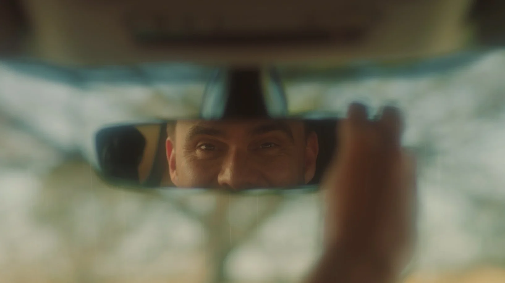 Homem olhando para o espelho retrovisor do carro, com foco em seu rosto refletido.