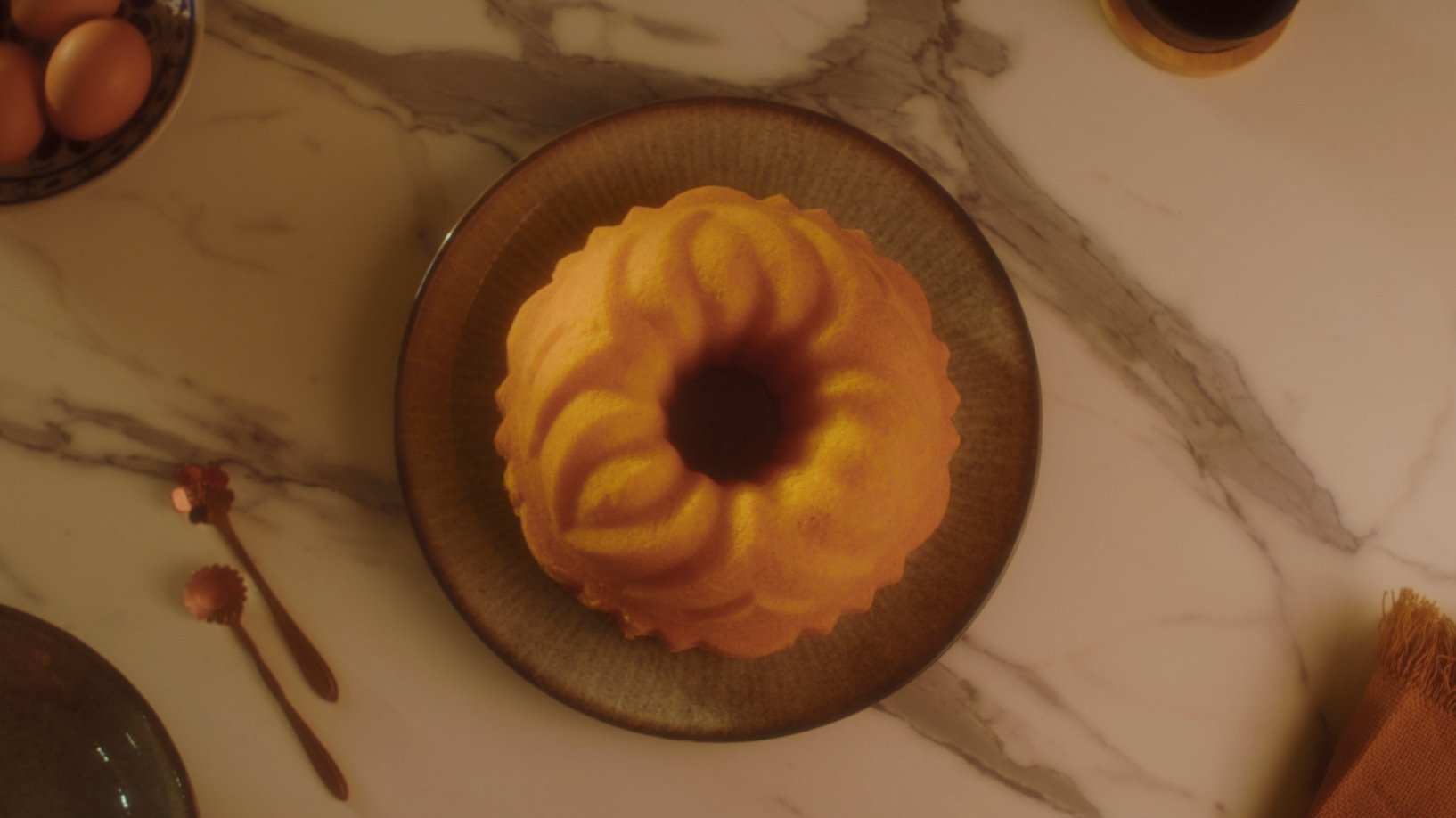 Bolo de cenoura com calda de chocolate em um prato escuro sobre uma mesa de mármore claro.