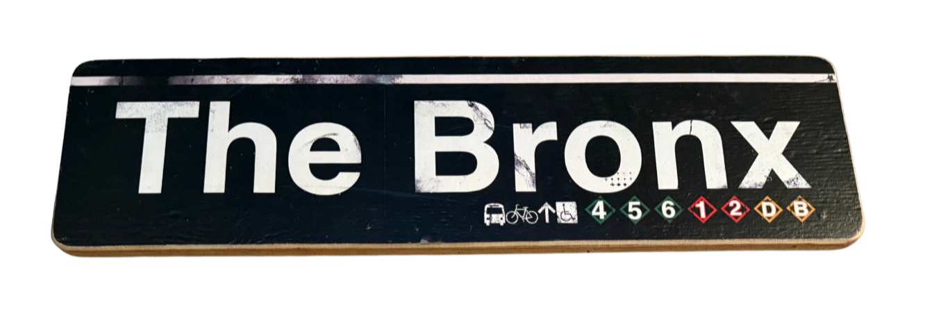 A black and white street sign reading 'The Bronx' with icons for public transportation, including bus, bike, wheelchair, and subway lines 4, 5, 6, 1, 2, D, and B.
