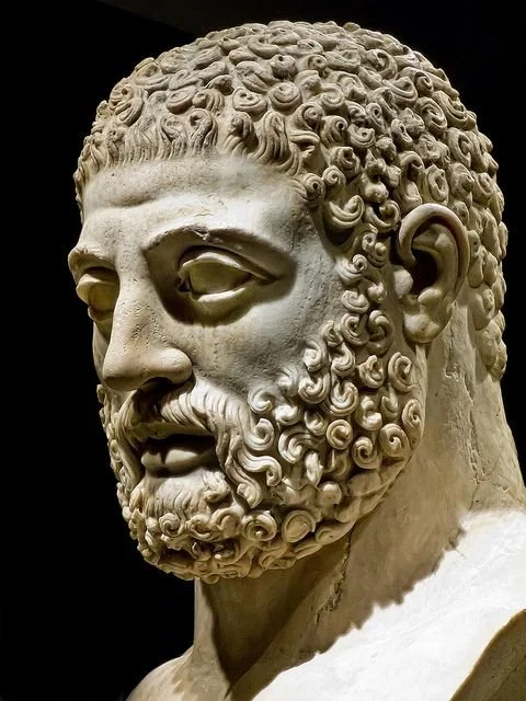 Close-up of an ancient Greek marble bust of a bearded man with curly hair and detailed facial features.
