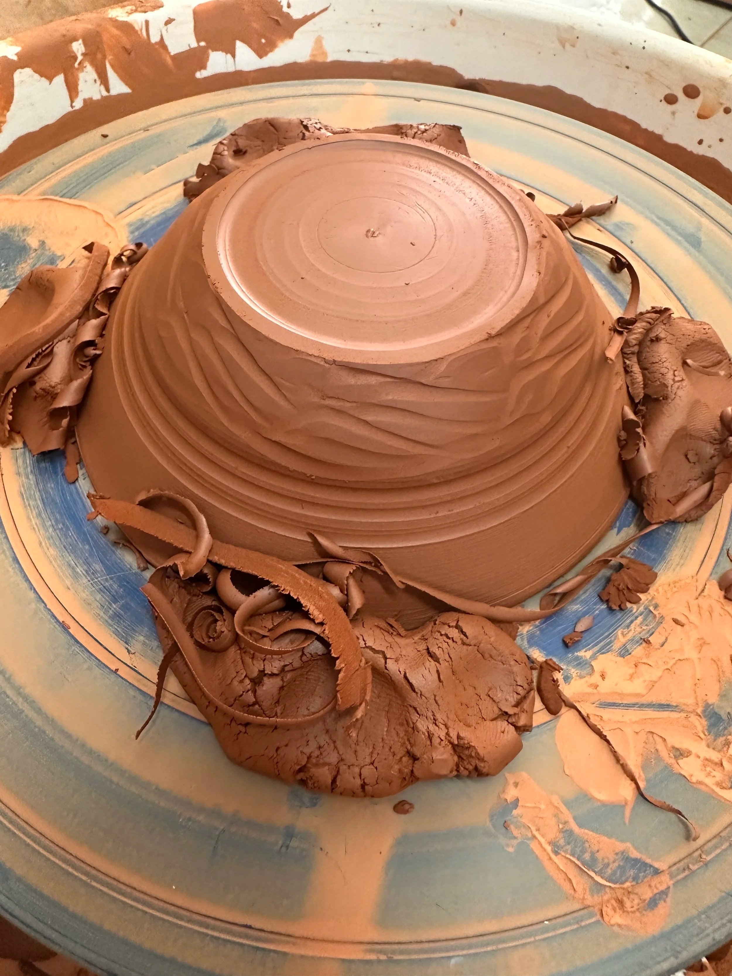 Trimming a terracotta bowl on the wheel, surrounded by clay shavings