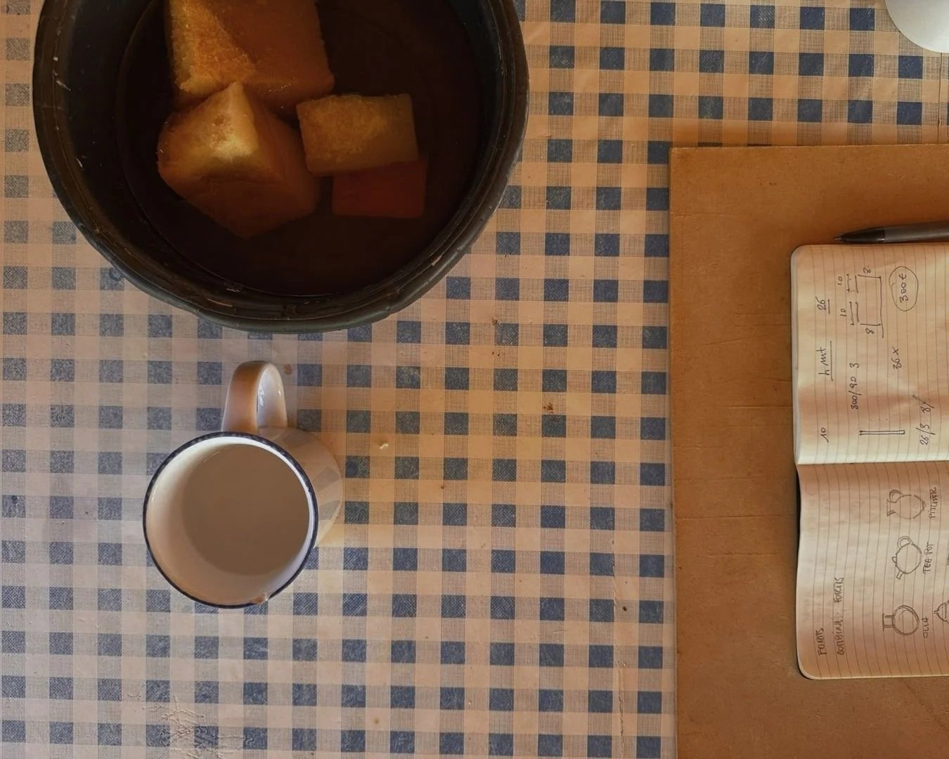 Notebook and coffee on a checked tablecloth, planning the retreats with our ceramicists