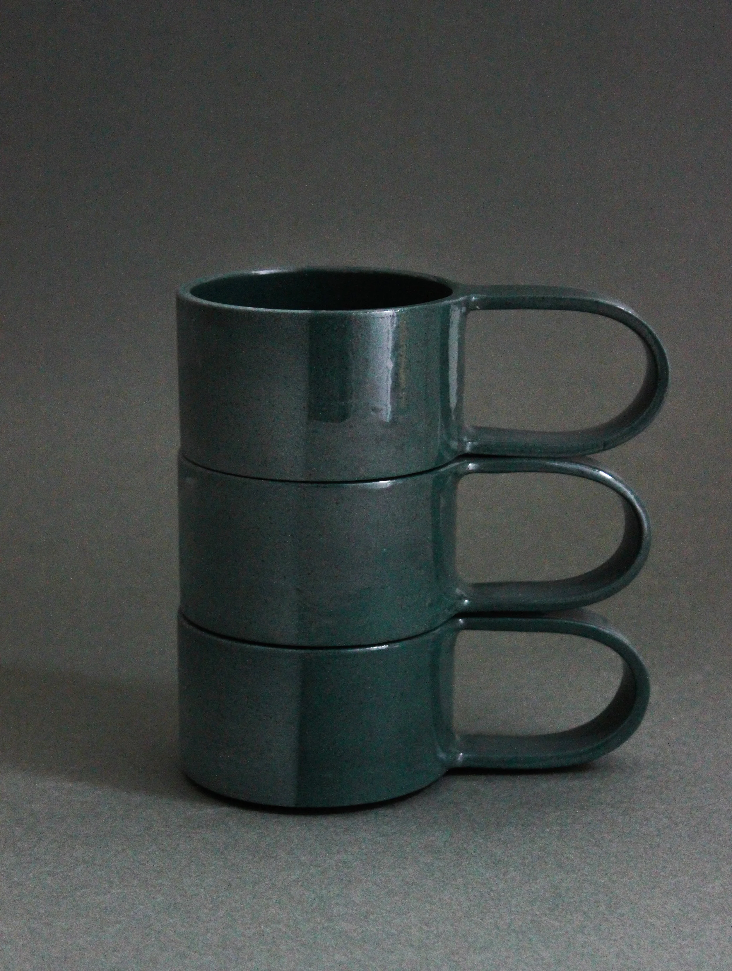 Stacked dark green ceramic mugs by Chiara Caselli
