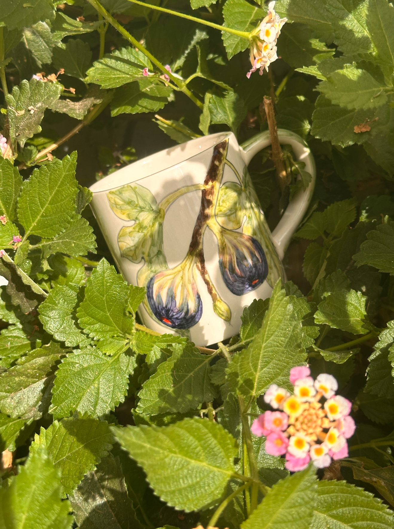 Hand-painted ceramic mug among lantana flowers