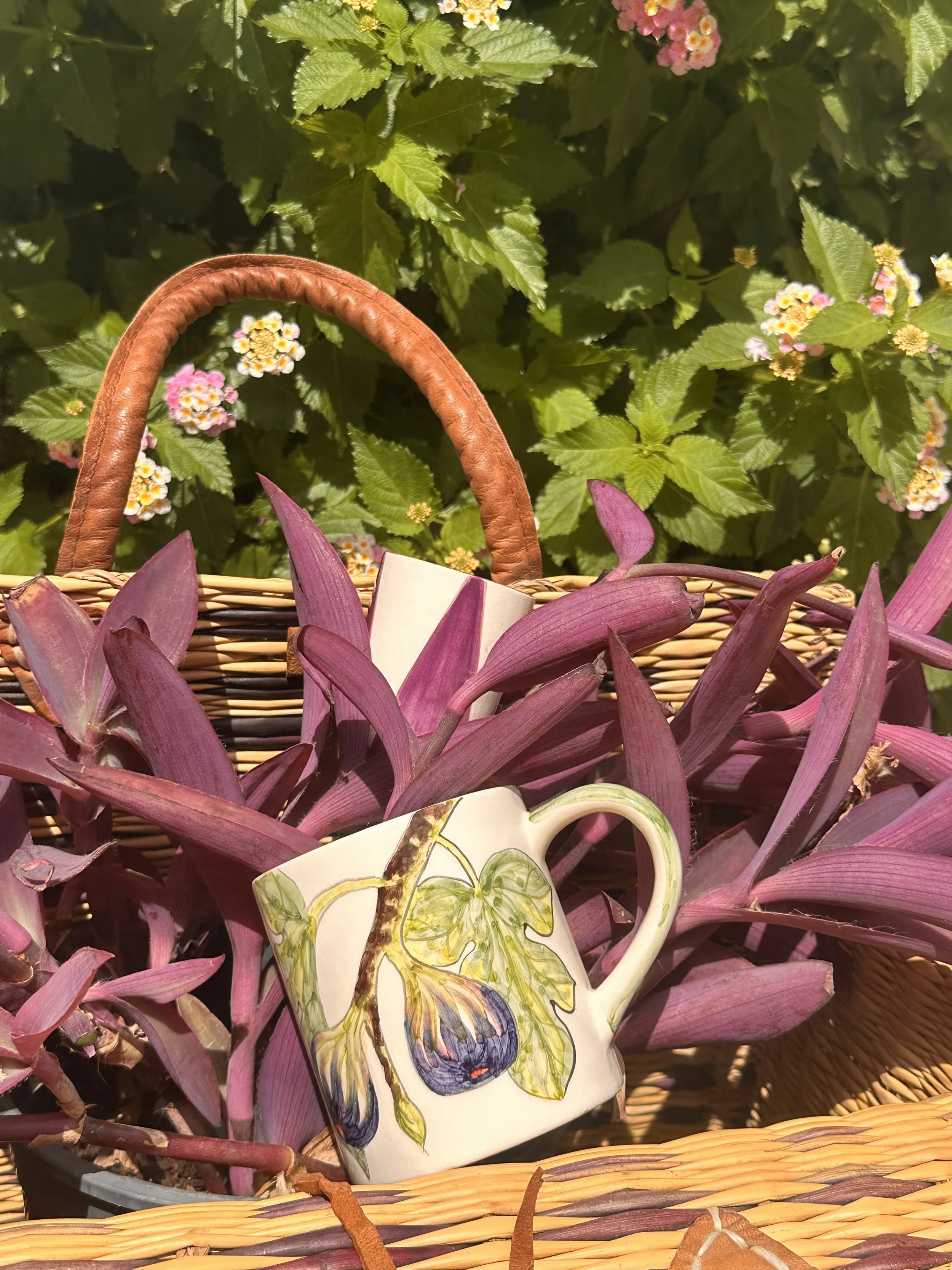 Hand-painted ceramic mug in a basket of purple leaves among flowers