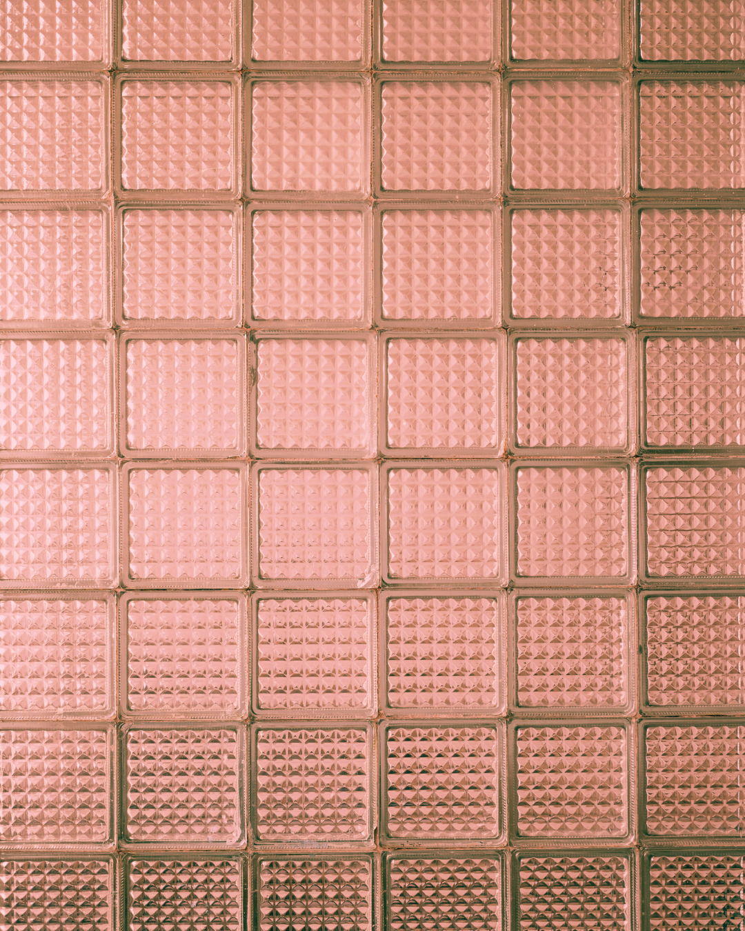 Close-up view of a wall made of pink glass blocks with textured, patterned surfaces.