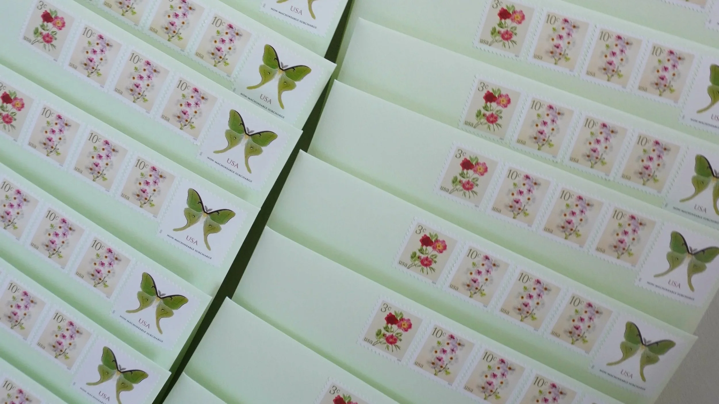 Sheets of US postage stamps with floral and butterfly designs. Some stamps feature pink flowers, others feature purple flowers, and there are butterfly stamps with green wings.