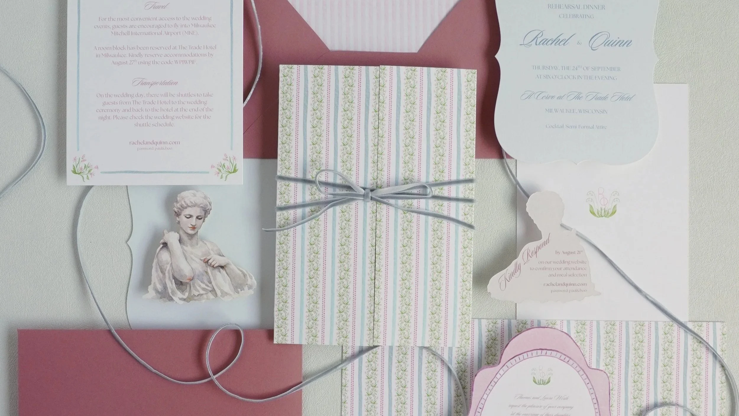 A collection of wedding invitation cards, a wrapped gift with a ribbon, and a small vintage statue of a woman, laid out on a white surface with pink and blue accents.