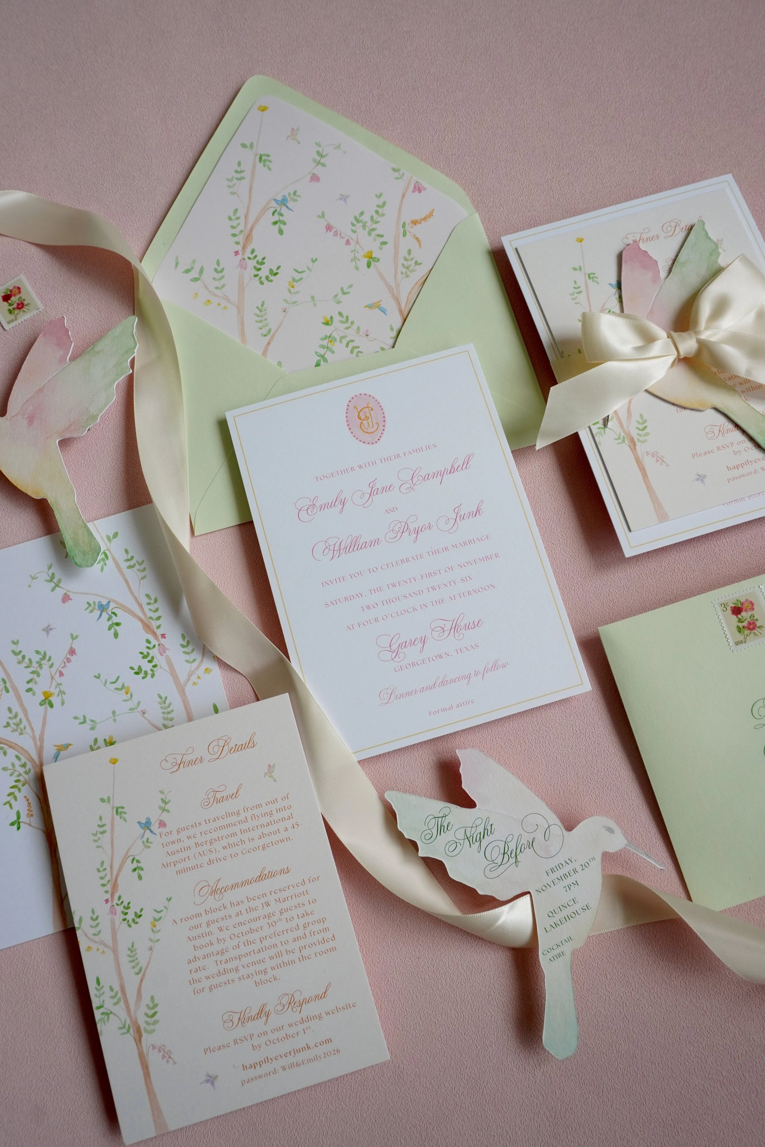 A wedding invitation set with floral and bird illustrations, featuring a green envelope, RSVP card, and a cream-colored ribbon tied into a bow, all arranged on a pink background.