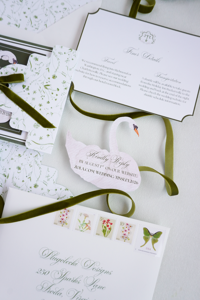Wedding invitation suite with floral and swan motifs, featuring a swan-shaped RSVP card, green ribbon, postage stamps with flowers and a butterfly, and elegant script lettering.