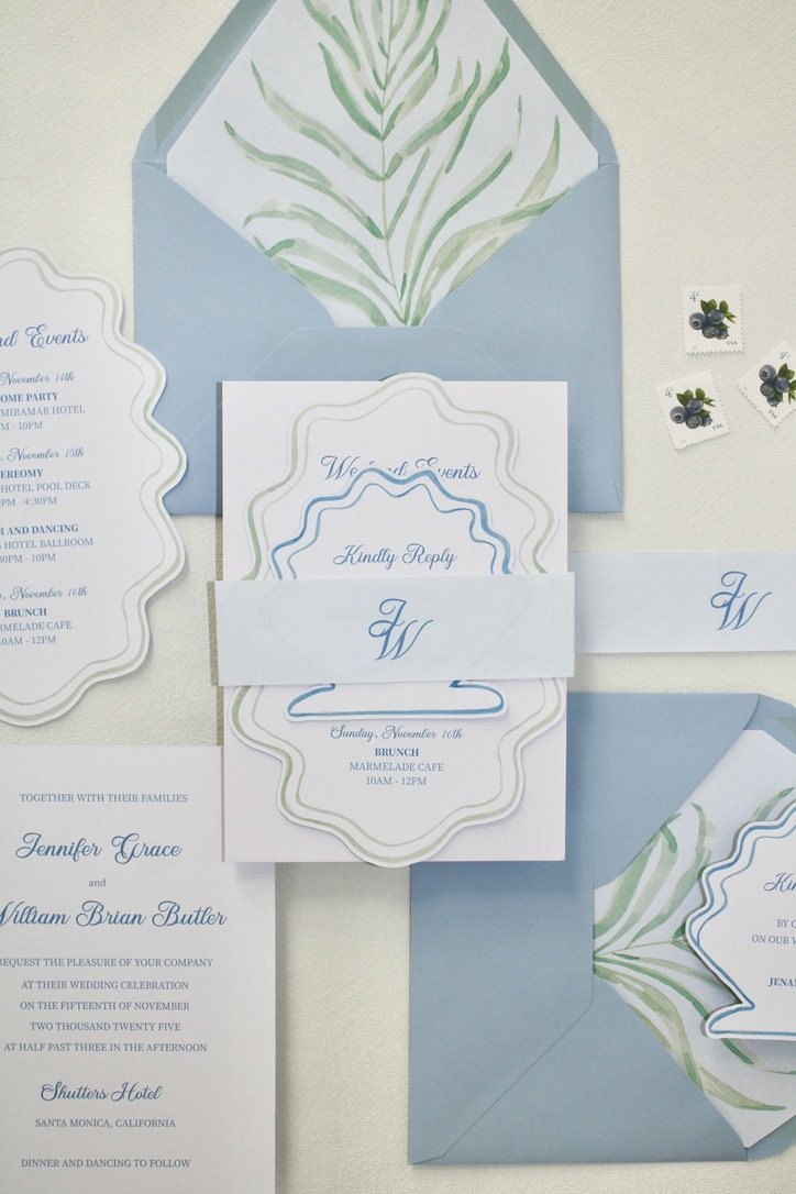Wedding invitation suite with matching RSVP card, details card, and envelopes in pastel blue, white, and green with botanical accents.