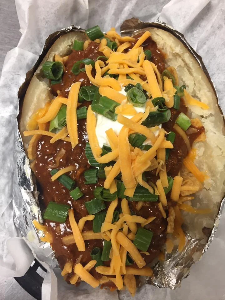 Baked potato topped with chili, shredded cheddar cheese, chopped green onions, and sour cream.
