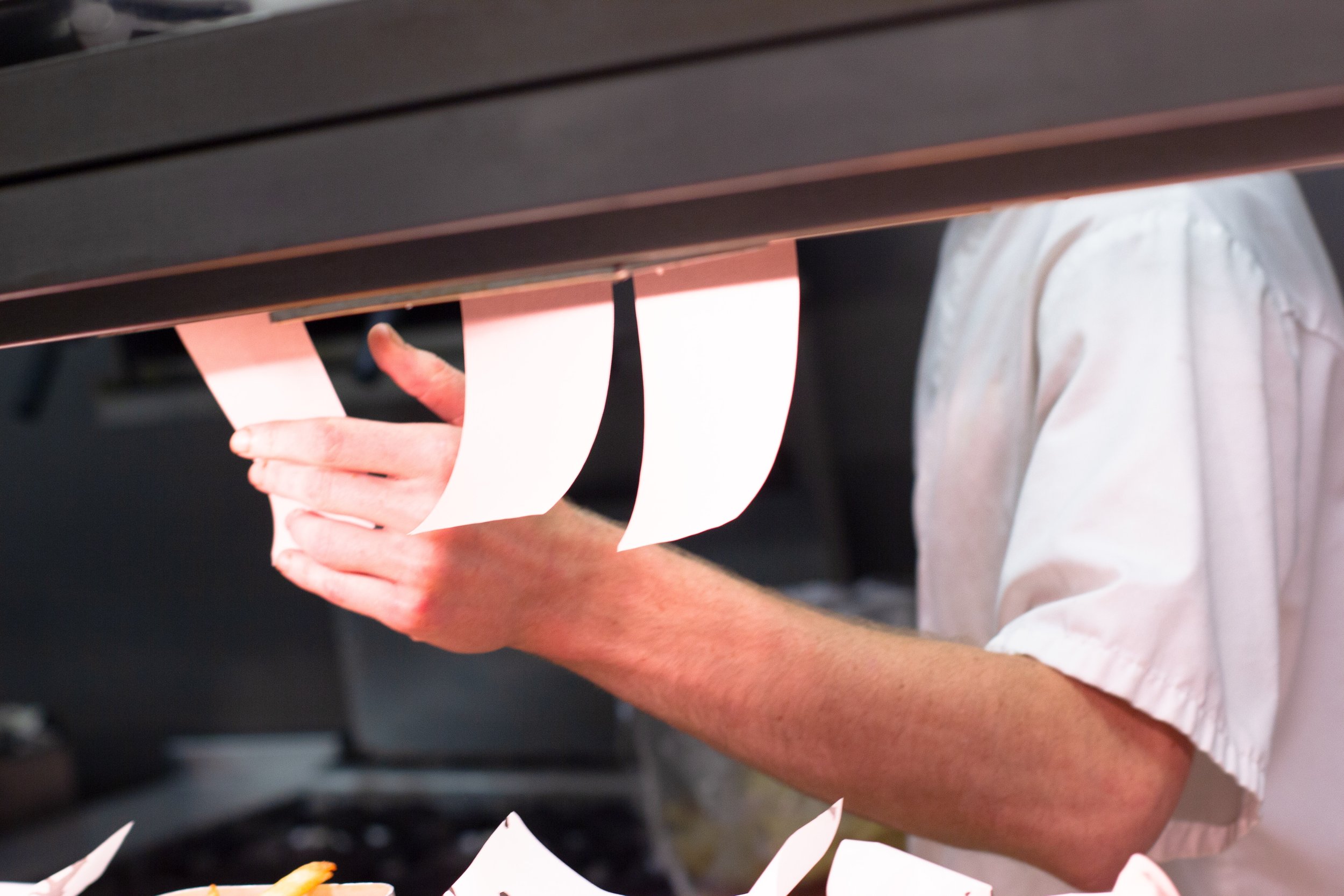 A person with a light-colored shirt is holding a strip of paper near an oven or a heating element, where the paper is being burned or singed. The photo shows the person's hand and part of their arm, with a dark surface or appliance above.