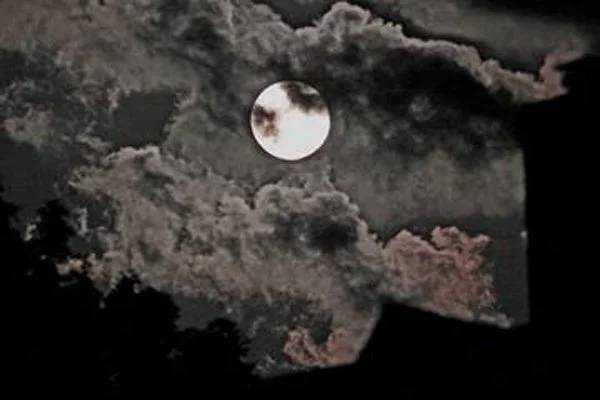 Full moon behind dark clouds in a night sky.