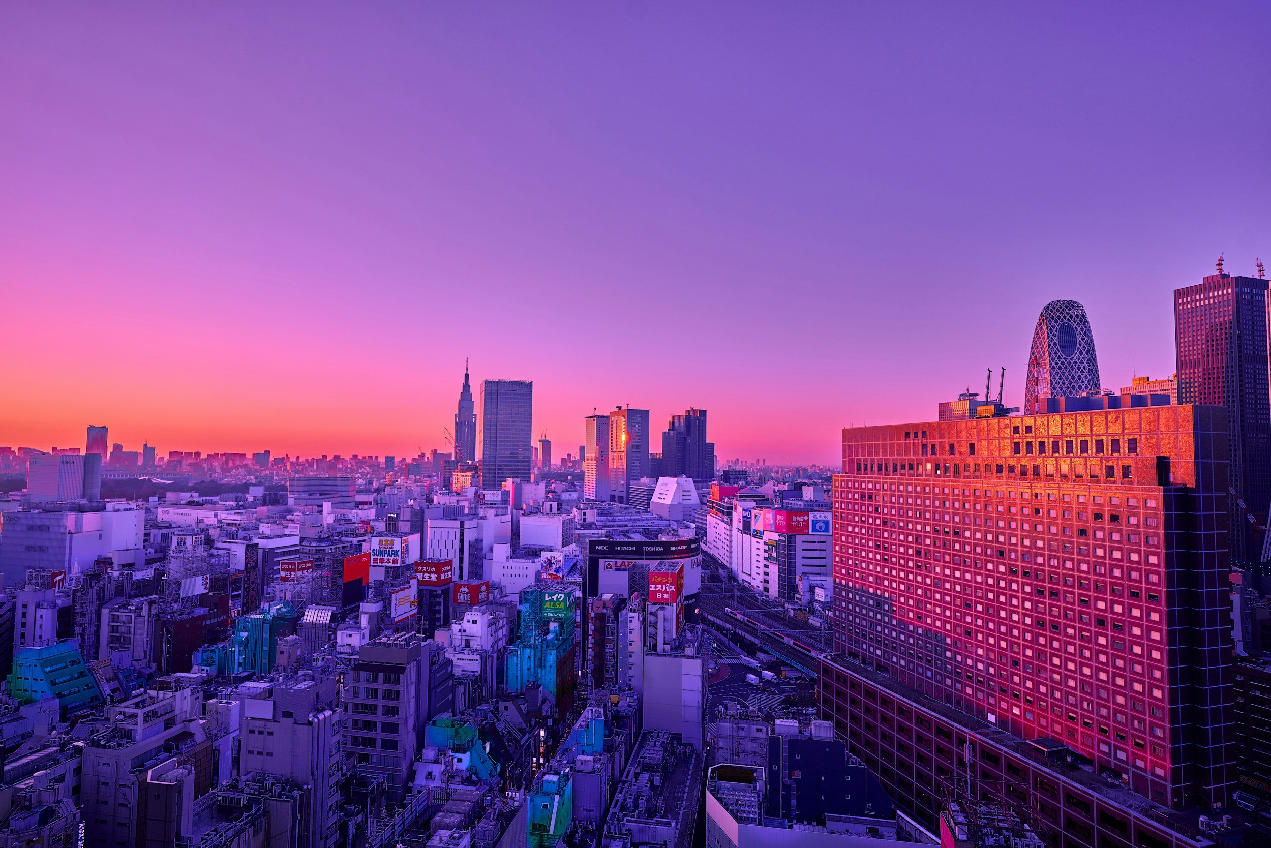 Skyline of a city at sunset with tall buildings and colorful sky in shades of purple, pink, and orange.