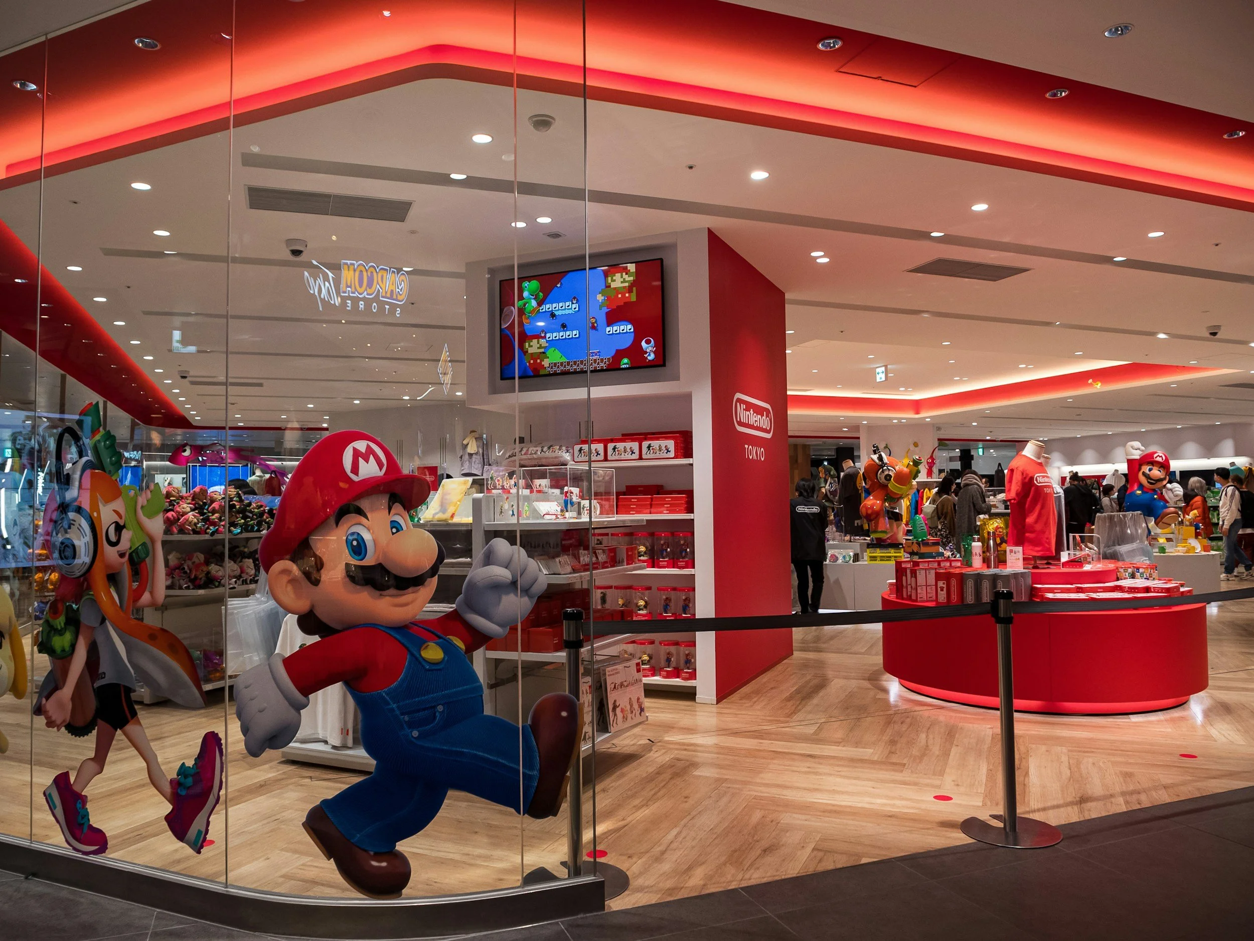 Nintendo Store with life-size Mario and Luigi figures, shelves of Nintendo merchandise, and a digital display showing Mario and Luigi. Store features red and white branding elements.