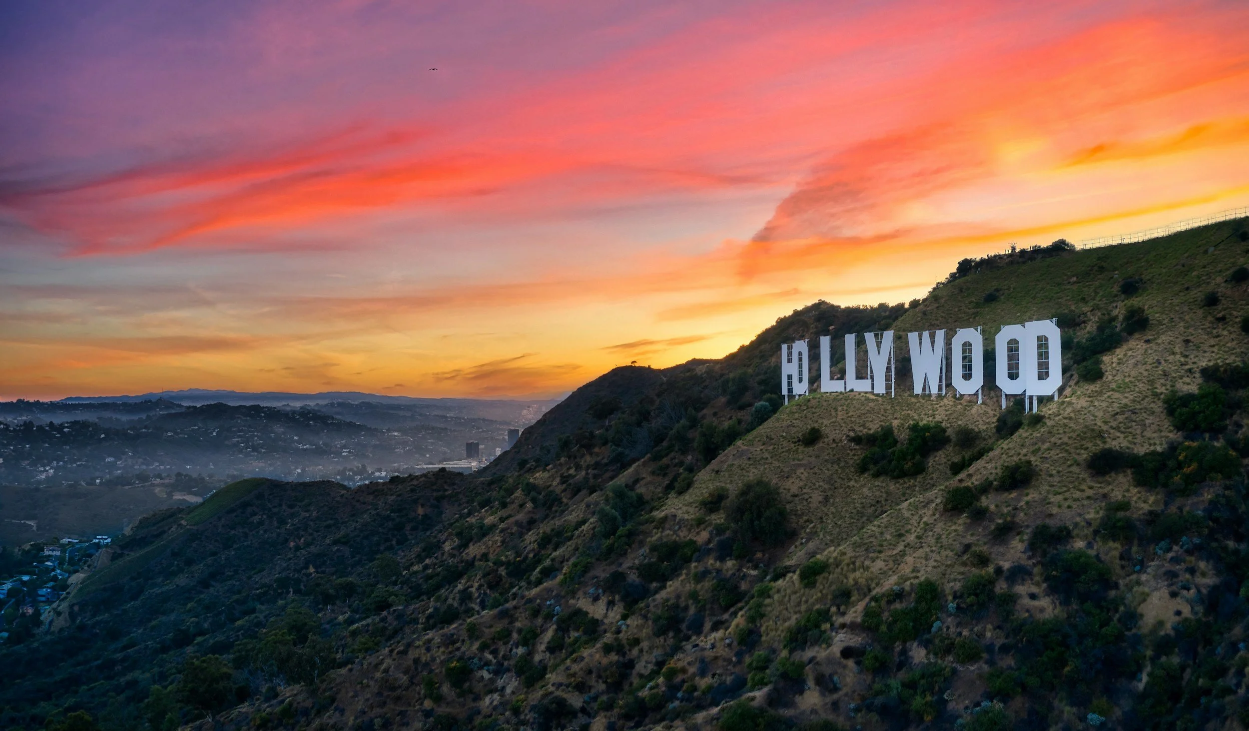 View of the Hollywood sign on a hillside at sunset, with colorful sky in shades of pink, orange, and purple.