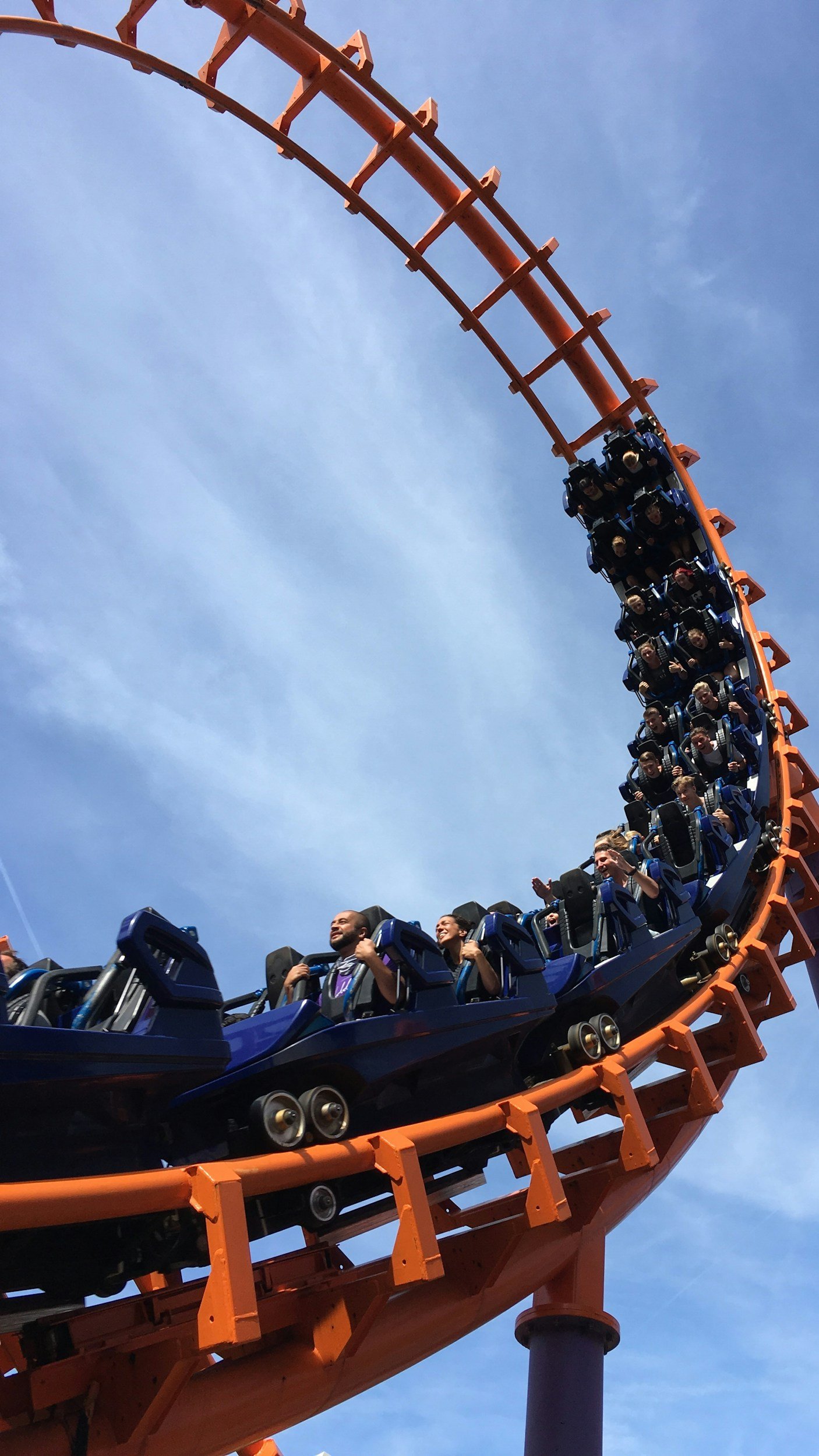 People riding a roller coaster at an amusement park, with the coaster track curving sharply against a blue sky.