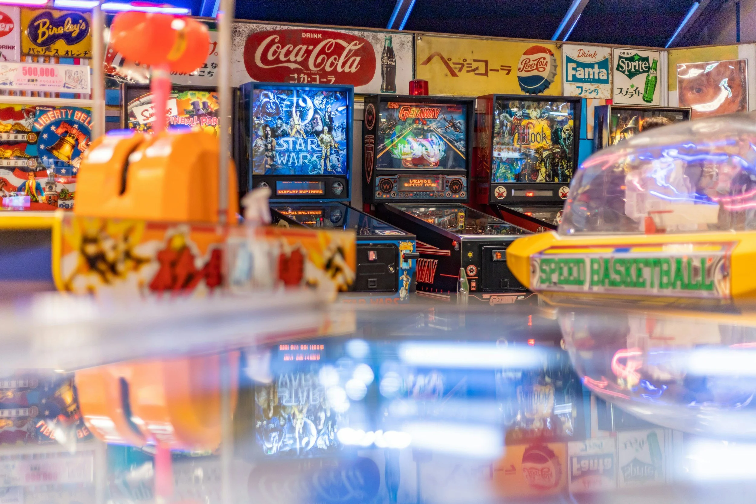 A close-up image of a pinball arcade with several pinball machines, arcade signs, and vintage advertisements on the wall.