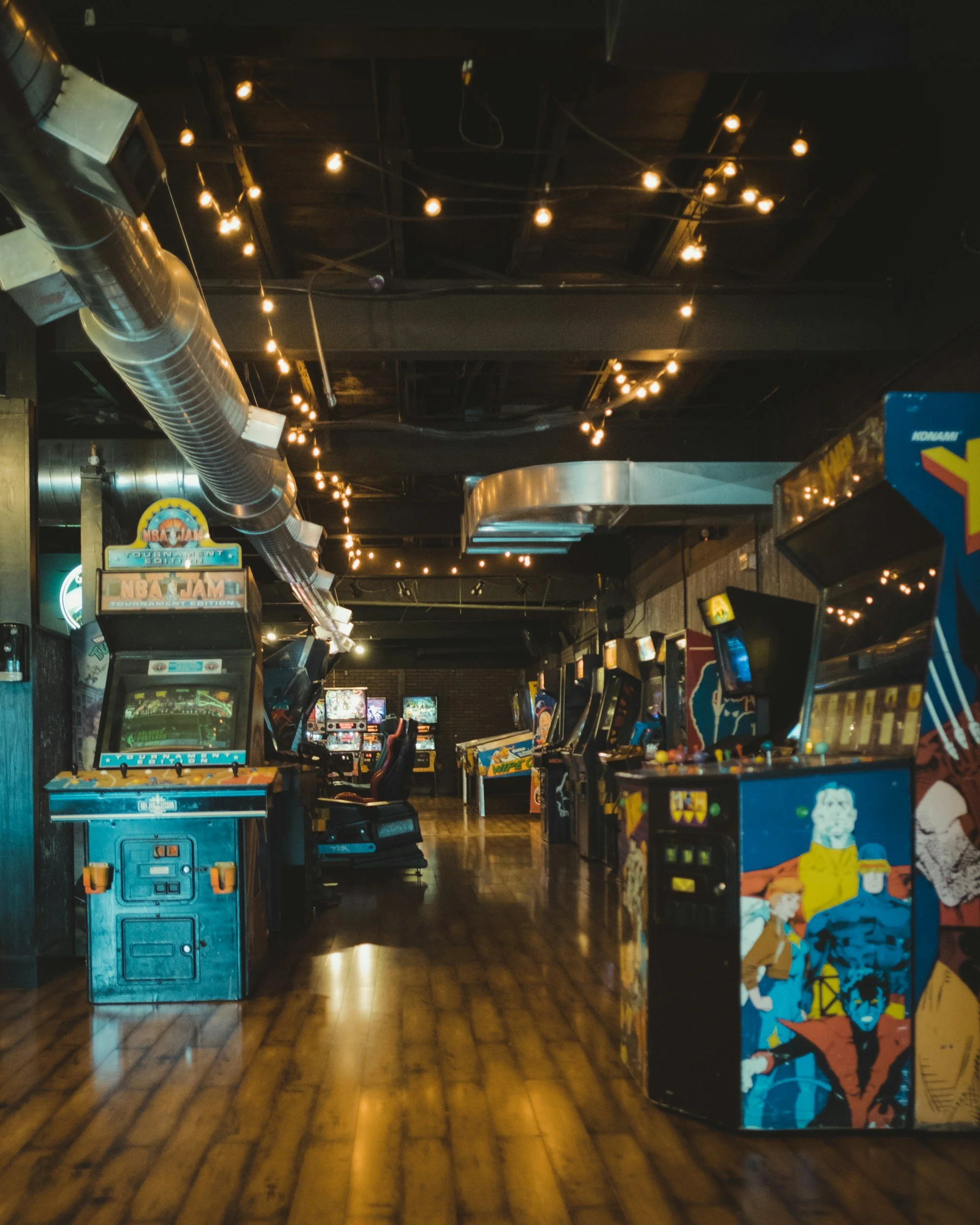 Inside an arcade with arcade machines, string lights hanging from the ceiling, and wooden floors.