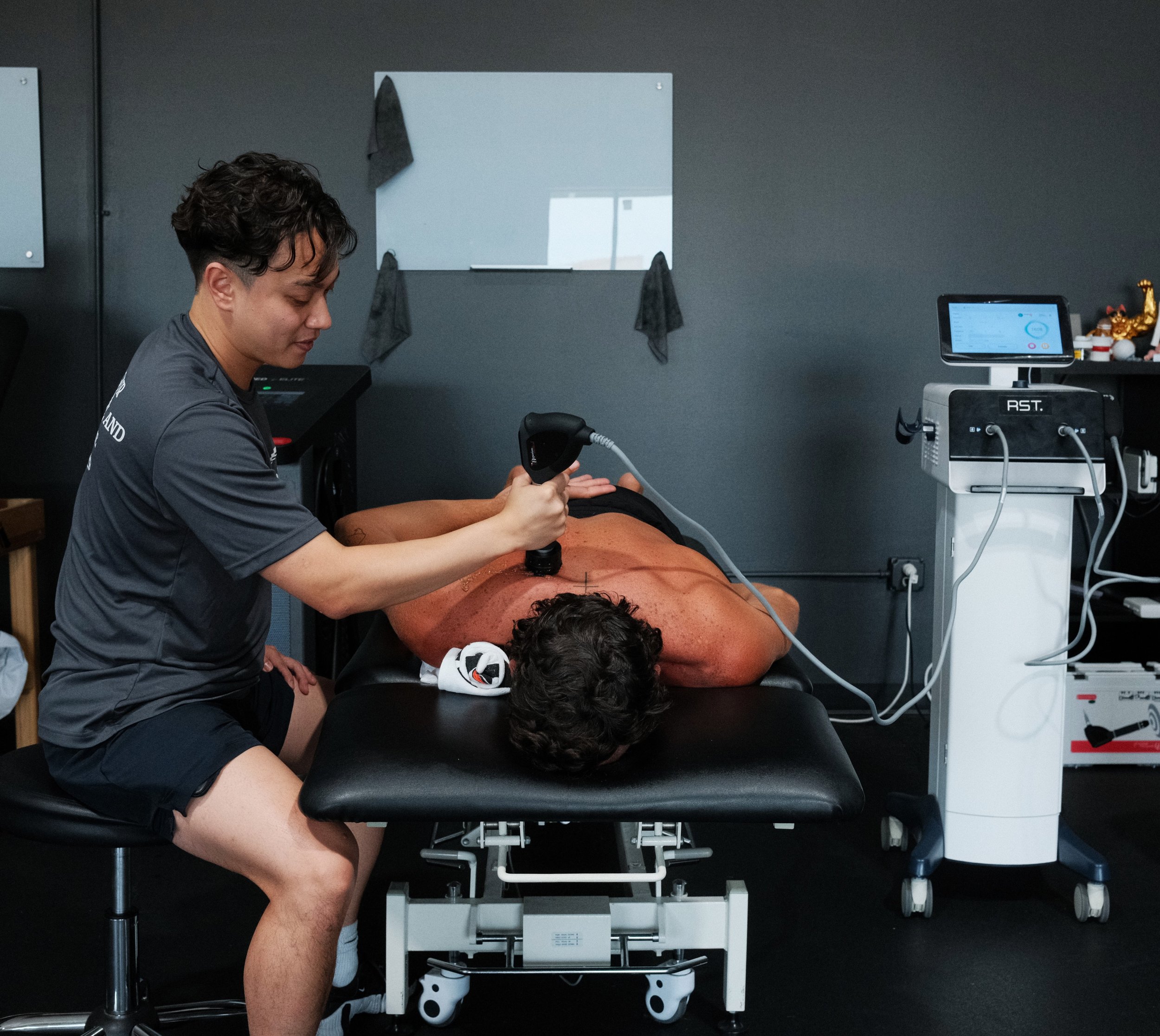 Chiropractor using a handheld therapy device on a patient’s back in a treatment room