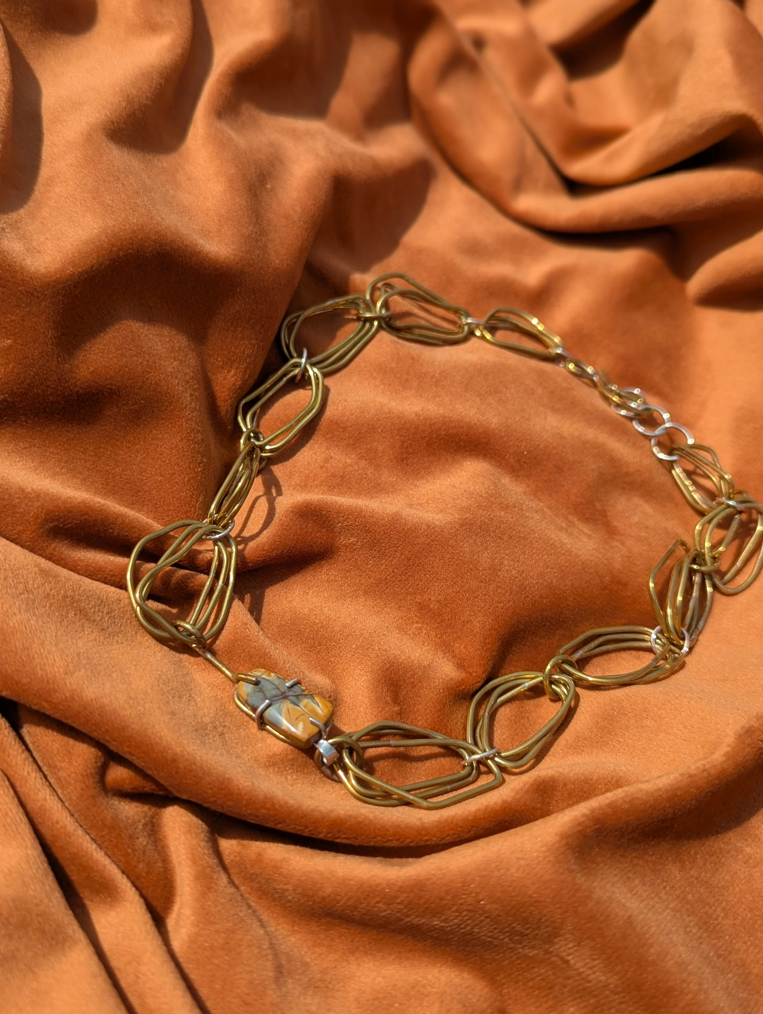 Gold and silver chain necklace with decorative links and beads, lying on a brown satin fabric with a soft sheen and folds.