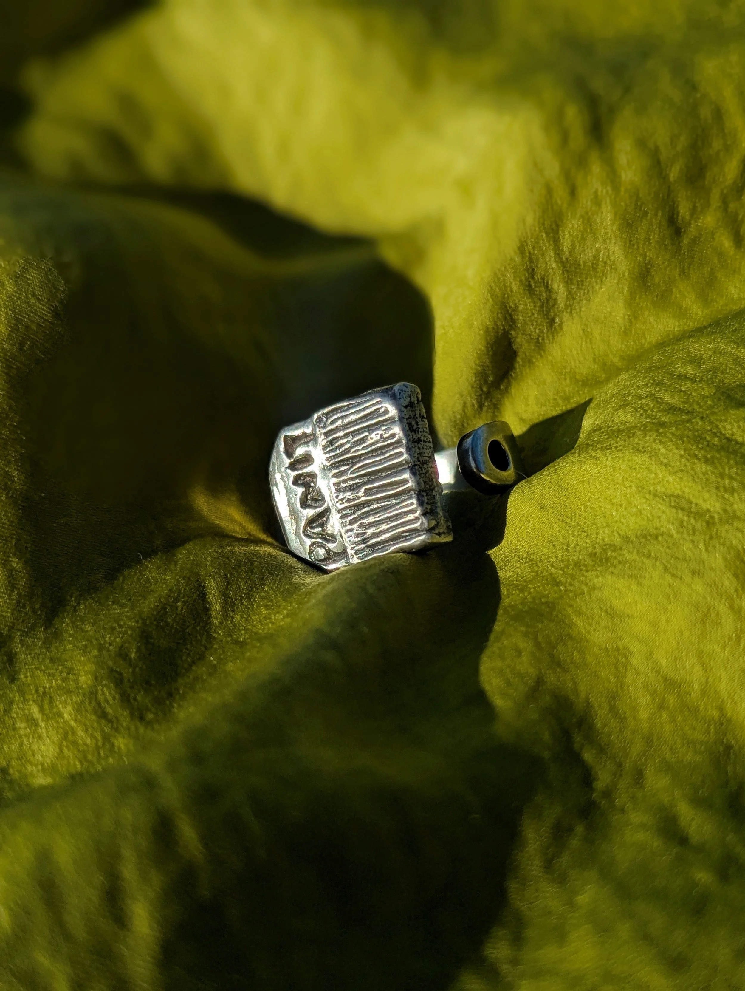 Close-up of a green fabric or clothing with a metallic tag and a small part of a black object.