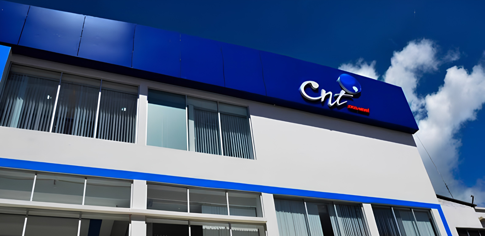 Edificio moderno con logo de CNT Telecomunicaciones en la parte superior, fachada blanca y detalles en azul, con ventanas y persianas verticales.