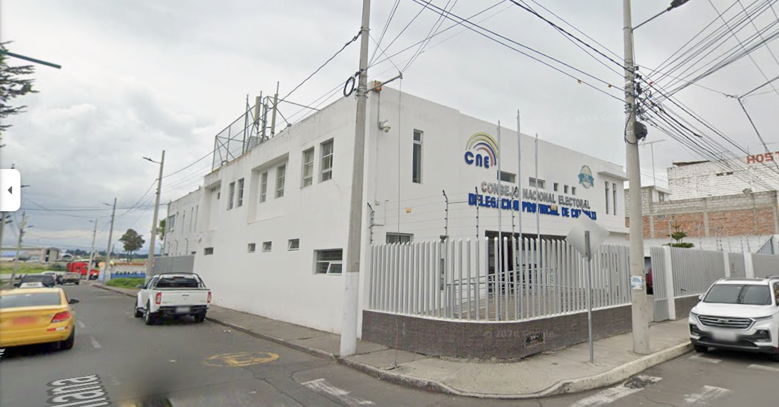 Edificio blanco con letreros del Consejo Nacional Electoral de México, en una esquina de la calle, con varios autos estacionados y cables eléctricos en el cielo.