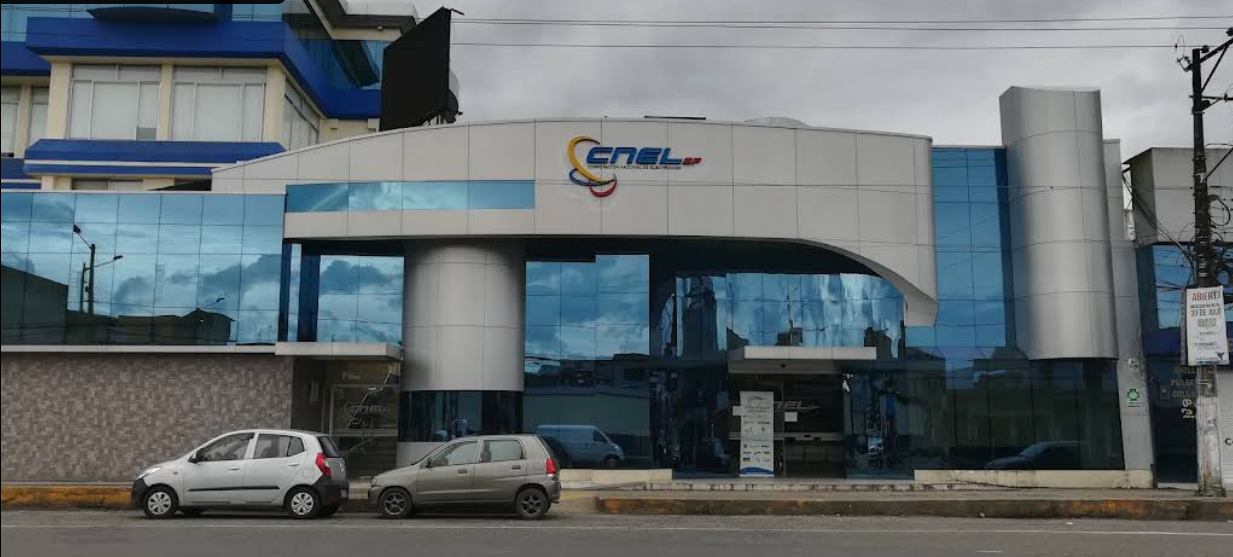 Edificio moderno con fachada de vidrio que alberga oficinas de ENEL, con dos coches estacionados delante y una señal en la acera.