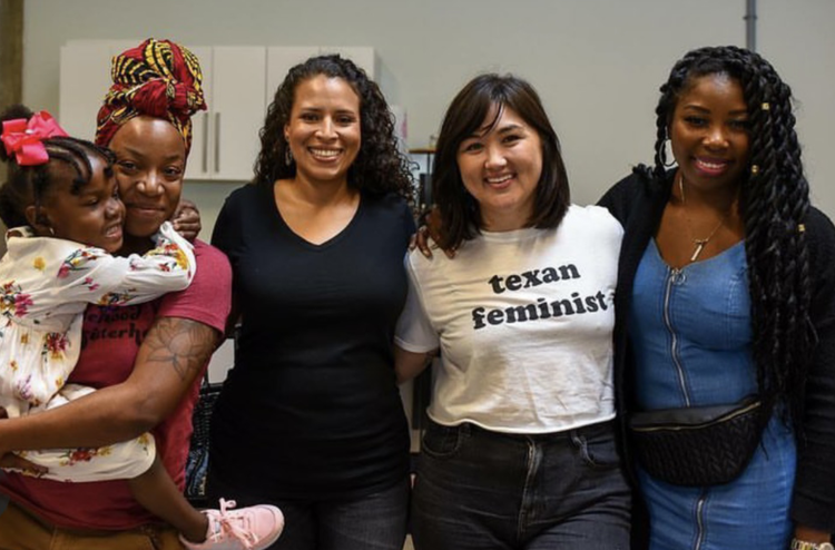Five women and a girl posing together indoors, smiling, with kitchen cabinets in the background.