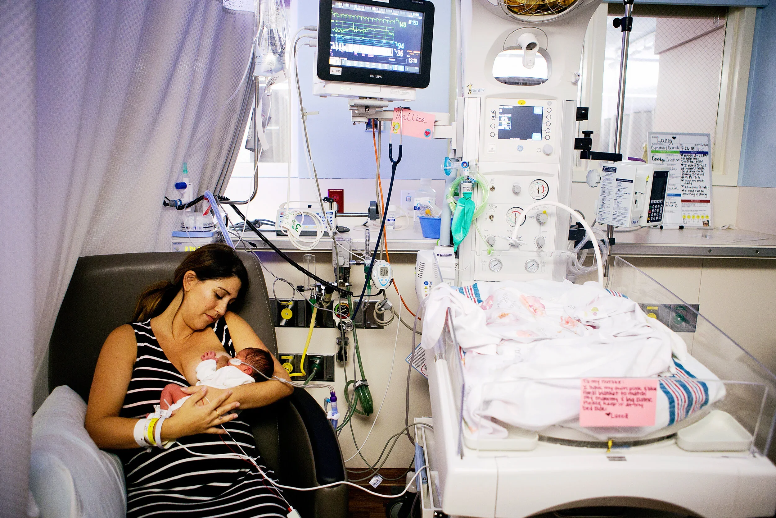 A woman holding a newborn baby in a hospital bed, surrounded by medical equipment.