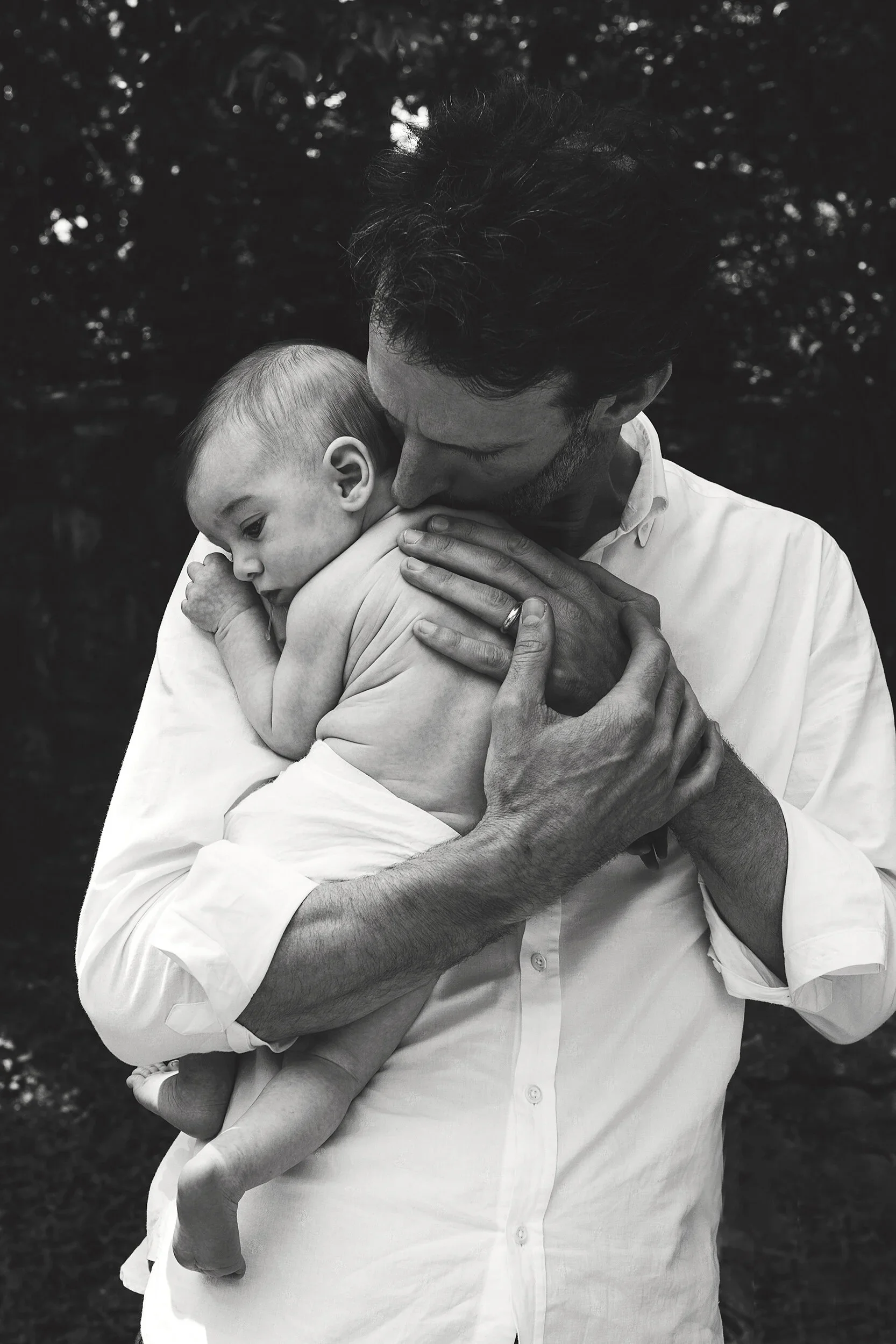 A man holding a young child in his arms, both embracing and sharing a moment of affection outdoors. The image is in black and white.