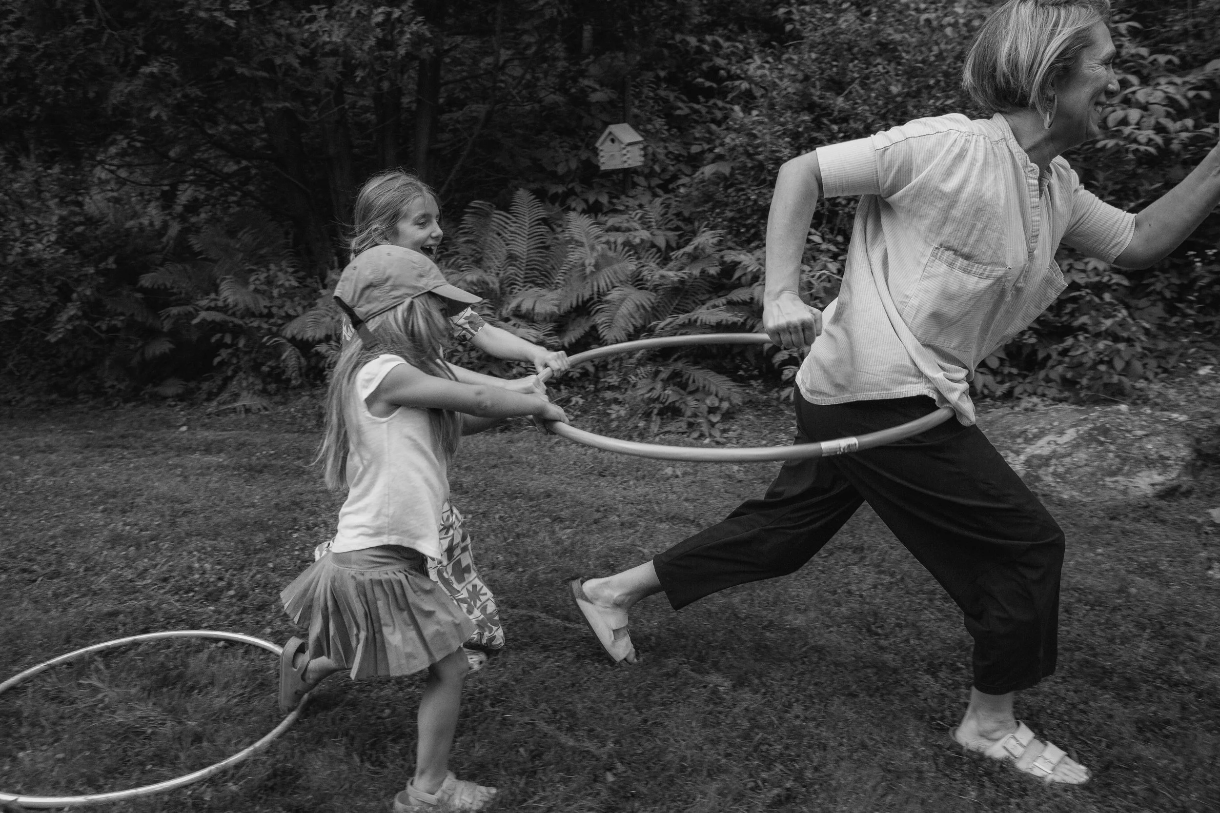 A woman and two children outdoor in a wooded area playing with hula hoops, black and white photo.